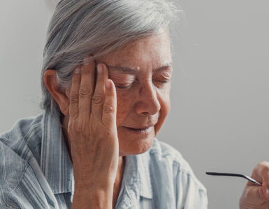 Elderly woman sits on a sofa at home suffering from a headache.