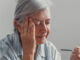 Elderly woman sits on a sofa at home suffering from a headache.