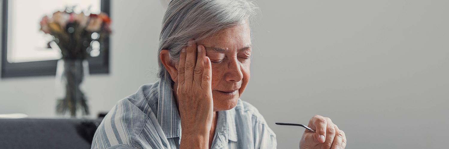 Elderly woman sits on a sofa at home suffering from a headache.