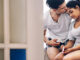 A woman sitting in a bathroom holding a pregnancy test and looking sad while a man kisses her forehead.