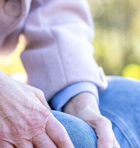 Elderly woman holding her leg on a bench.