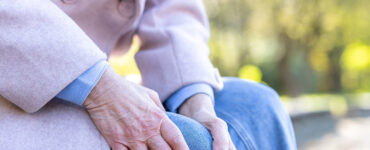 Elderly woman holding her leg on a bench.