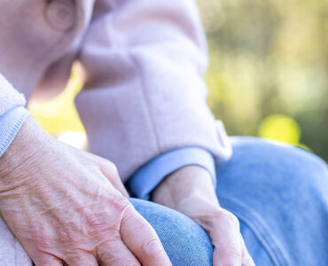 Elderly woman holding her leg on a bench.