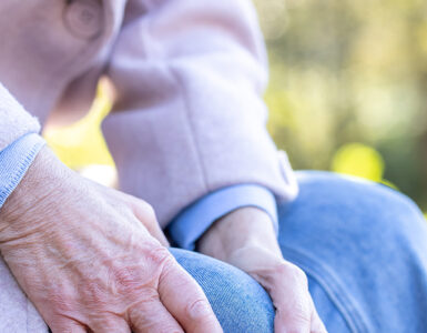 Elderly woman holding her leg on a bench.