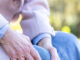 Elderly woman holding her leg on a bench.