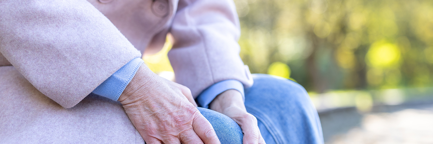 Elderly woman holding her leg on a bench.