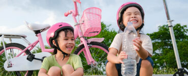 Little girls with helmets on taking a break from riding scooter and bike, drinking a water