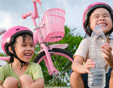 Little girls with helmets on taking a break from riding scooter and bike, drinking a water