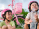 Little girls with helmets on taking a break from riding scooter and bike, drinking a water