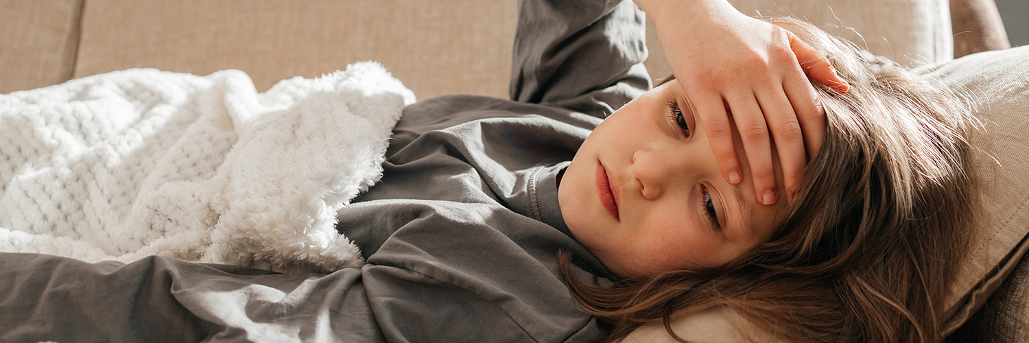 A young girl laying on a couch, holding her forehead while looking sickly.
