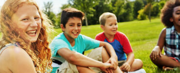 Kids sitting on lawn, smiling.