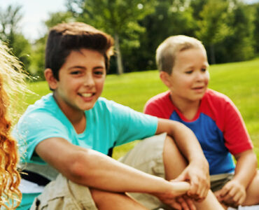 Kids sitting on lawn, smiling.
