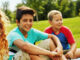 Kids sitting on lawn, smiling.