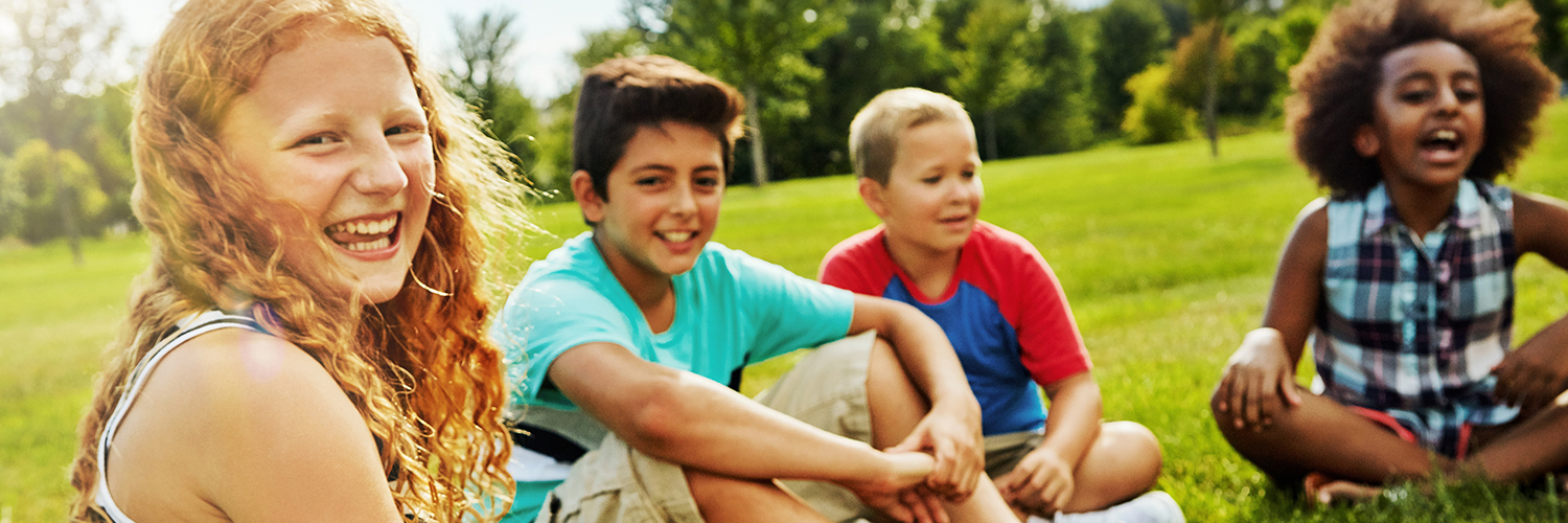 Kids sitting on lawn, smiling.