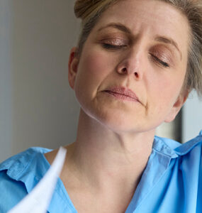 Menopausal Mature Woman Having Hot Flashes At Home Cooling Herself With Letters Or Documents