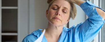 Menopausal Mature Woman Having Hot Flashes At Home Cooling Herself With Letters Or Documents