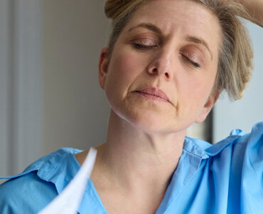 Menopausal Mature Woman Having Hot Flashes At Home Cooling Herself With Letters Or Documents