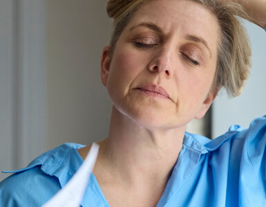 Menopausal Mature Woman Having Hot Flashes At Home Cooling Herself With Letters Or Documents