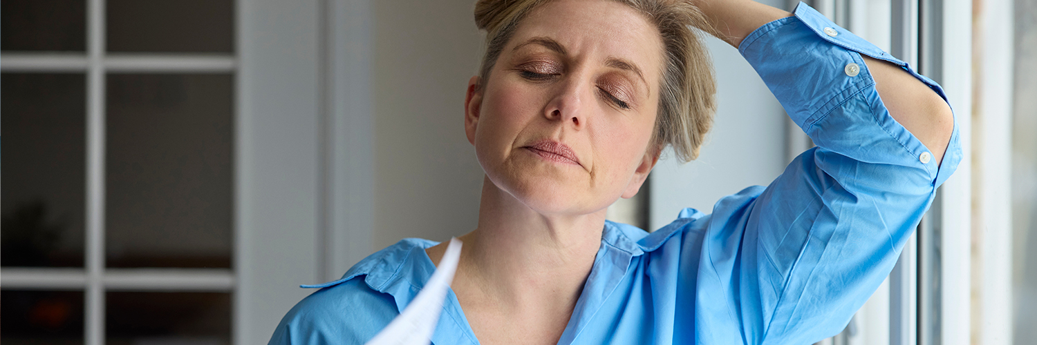 Menopausal Mature Woman Having Hot Flashes At Home Cooling Herself With Letters Or Documents