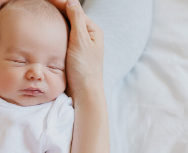 Sleeping newborn in hands of his mother.