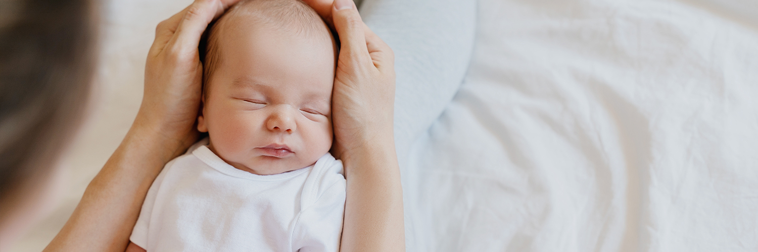 Sleeping newborn in hands of his mother.
