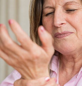 Senior woman clutching her wrist in pain, showing discomfort from arthritis or joint inflammation.