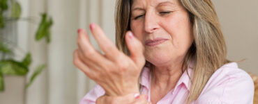 Senior woman clutching her wrist in pain, showing discomfort from arthritis or joint inflammation.