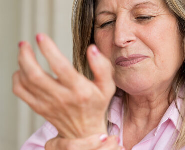 Senior woman clutching her wrist in pain, showing discomfort from arthritis or joint inflammation.