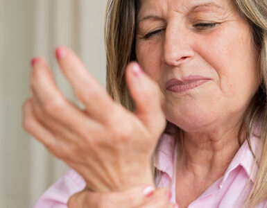 Senior woman clutching her wrist in pain, showing discomfort from arthritis or joint inflammation.