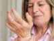Senior woman clutching her wrist in pain, showing discomfort from arthritis or joint inflammation.