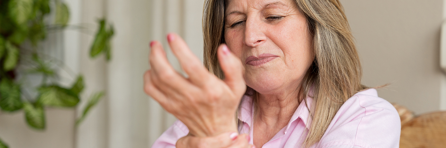 Senior woman clutching her wrist in pain, showing discomfort from arthritis or joint inflammation.