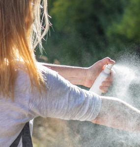 A women standing outdoors, spraying herself to protect from ticks.