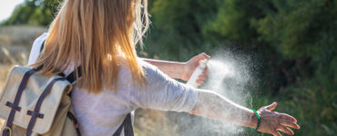 A women standing outdoors, spraying herself to protect from ticks.