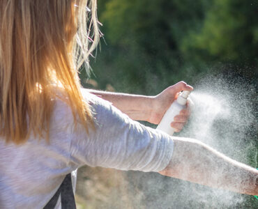 A women standing outdoors, spraying herself to protect from ticks.