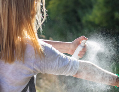 A women standing outdoors, spraying herself to protect from ticks.