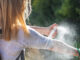 A women standing outdoors, spraying herself to protect from ticks.