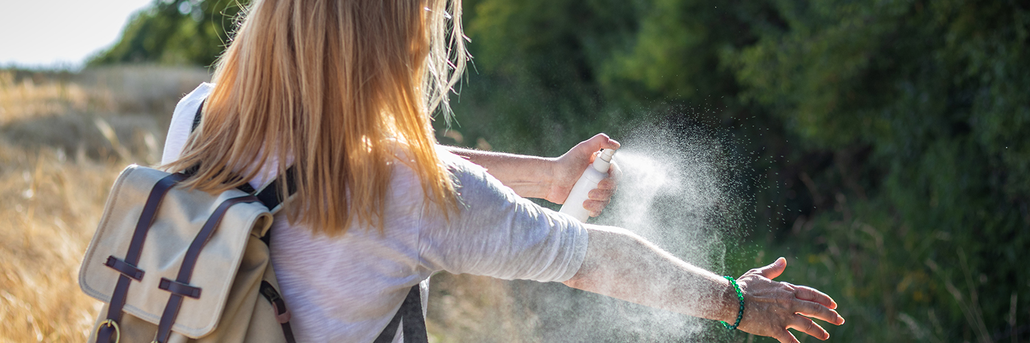 A women standing outdoors, spraying herself to protect from ticks.