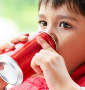 A young boy wearing a red coat and sipping from a red soda can.