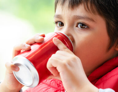 A young boy wearing a red coat and sipping from a red soda can.