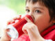 A young boy wearing a red coat and sipping from a red soda can.