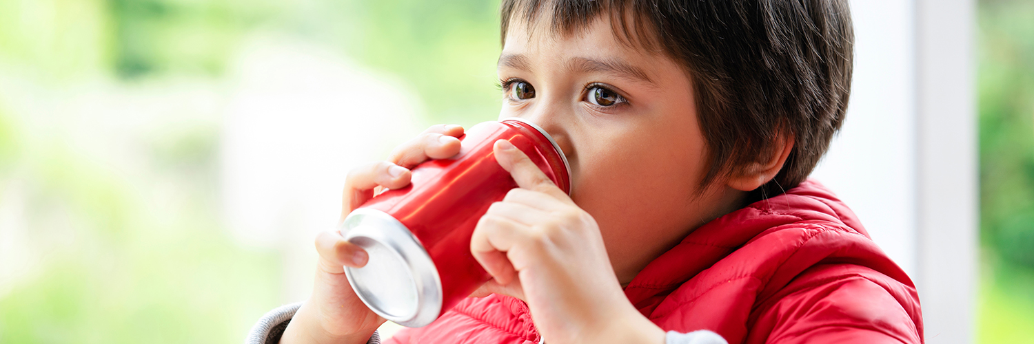 A young boy wearing a red coat and sipping from a red soda can.
