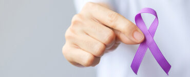 A hand holding up a purple ribbon for overdose awareness month.
