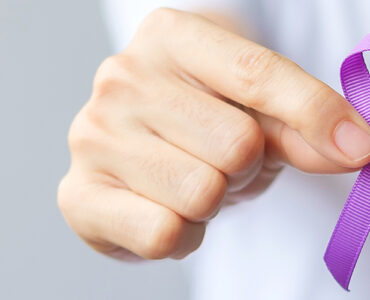 A hand holding up a purple ribbon for overdose awareness month.