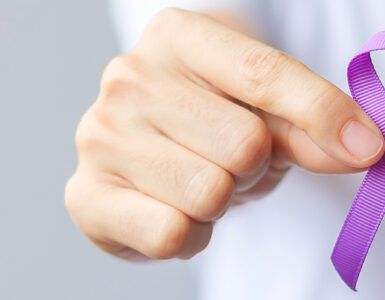 A hand holding up a purple ribbon for overdose awareness month.