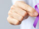 A hand holding up a purple ribbon for overdose awareness month.