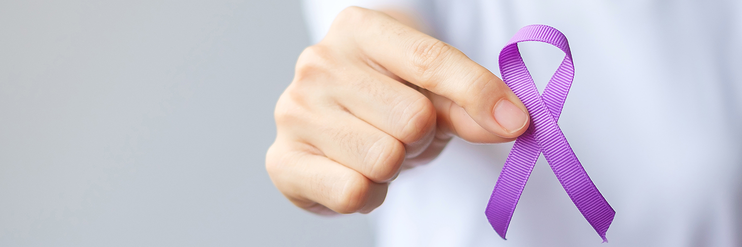 A hand holding up a purple ribbon for overdose awareness month.
