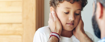 A young boy being consoled by his father while looking anxious.