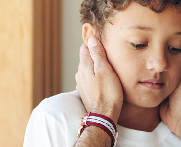 A young boy being consoled by his father while looking anxious.