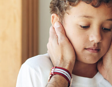 A young boy being consoled by his father while looking anxious.