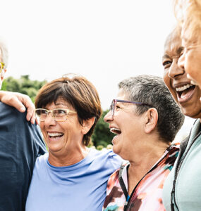 A group of adults ages 65 and up, standing together in a semi-circle and laughing.